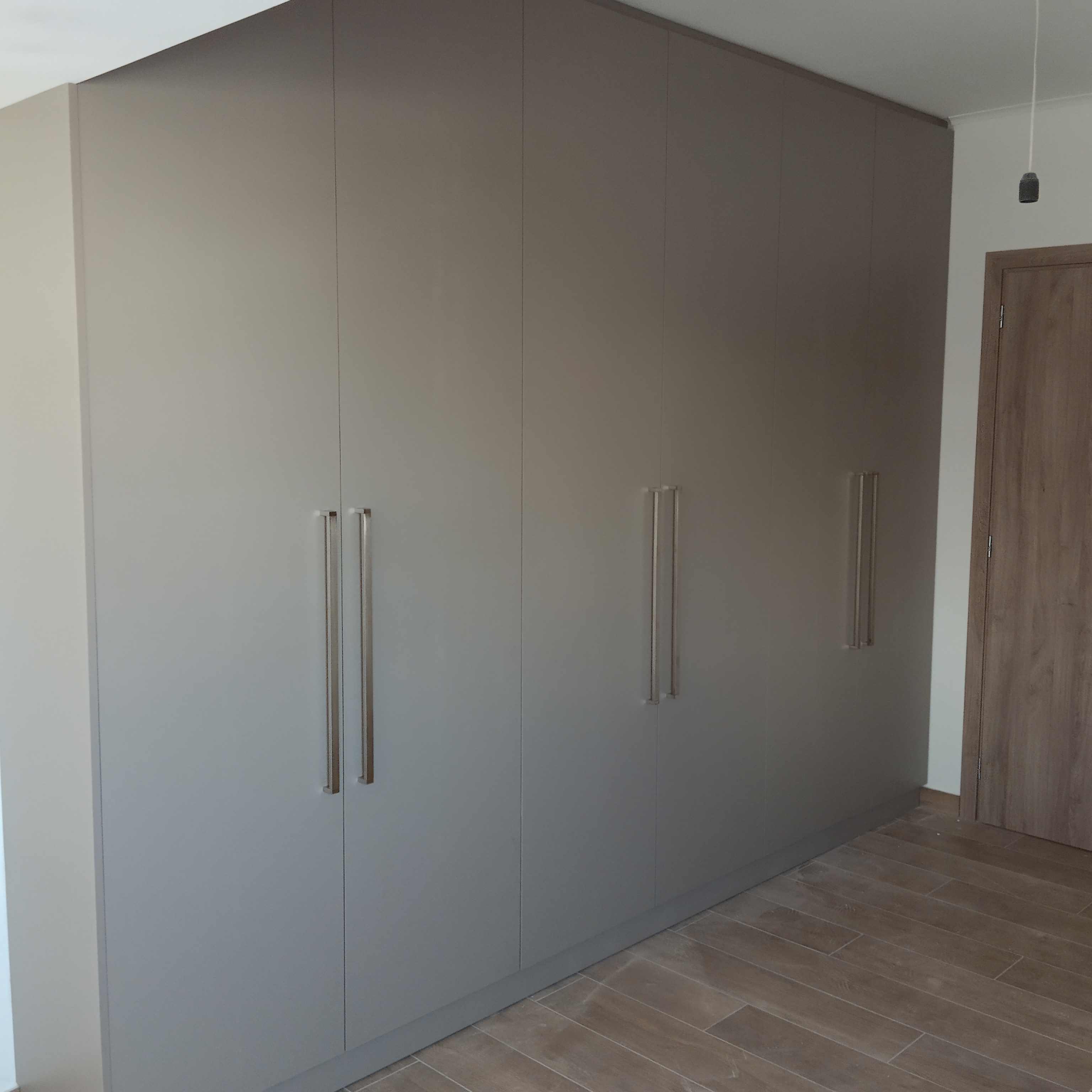 Εντοιχισμένη ντουλάπα από γκρι laminate με ανοιγόμενα φύλλα και μακριές μεταλλικές λαβές